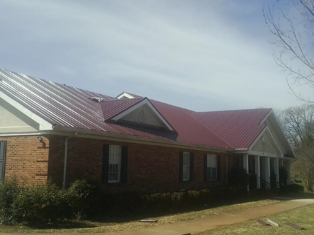 Red metal roof with gabled entries on a long brick building, from a Hail Damage Roof Repair job in Elk Creek