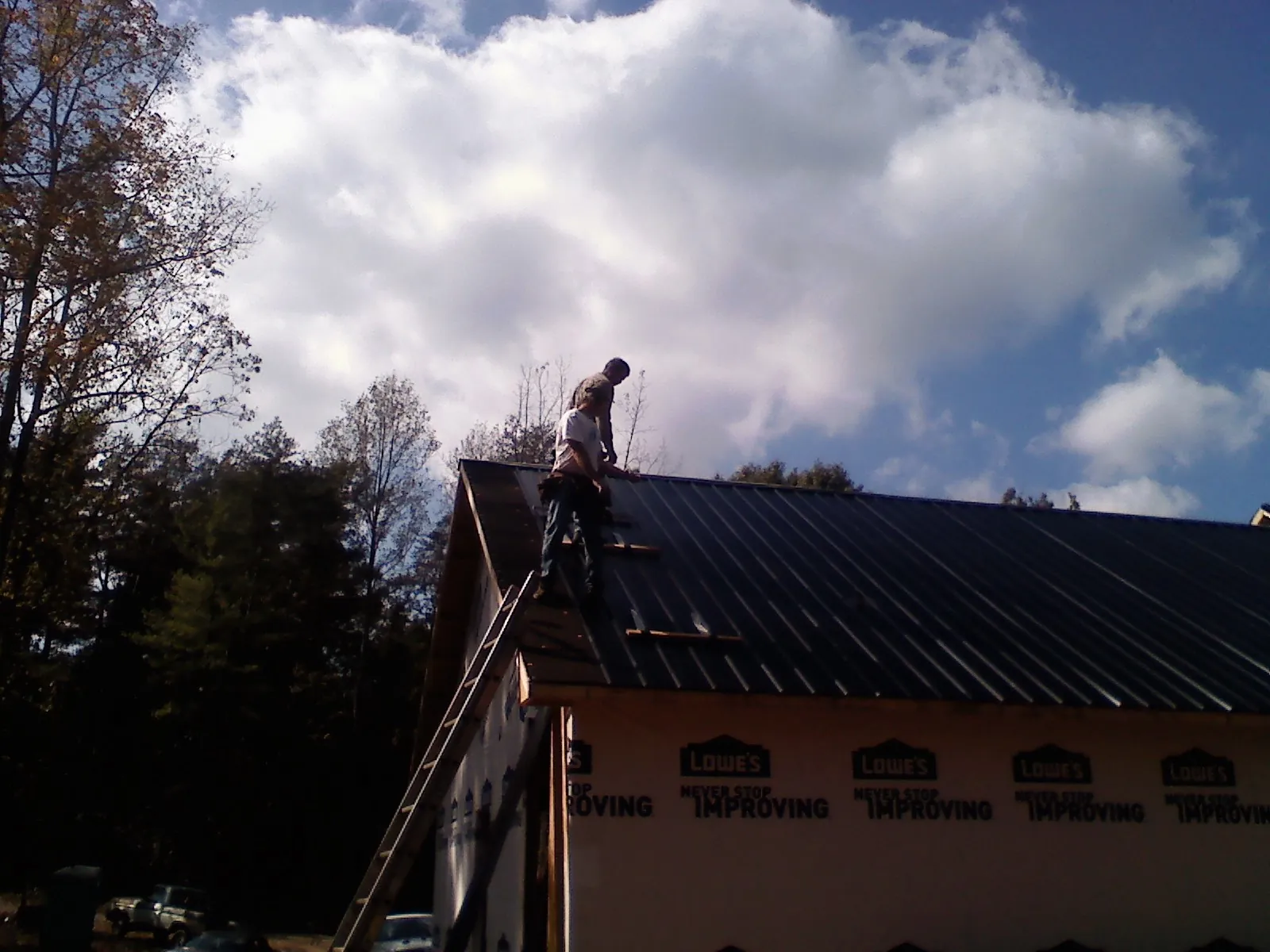 Roofer fastening dark metal panels high against a cloudy sky, from a Roof Inspection job in Elk Creek