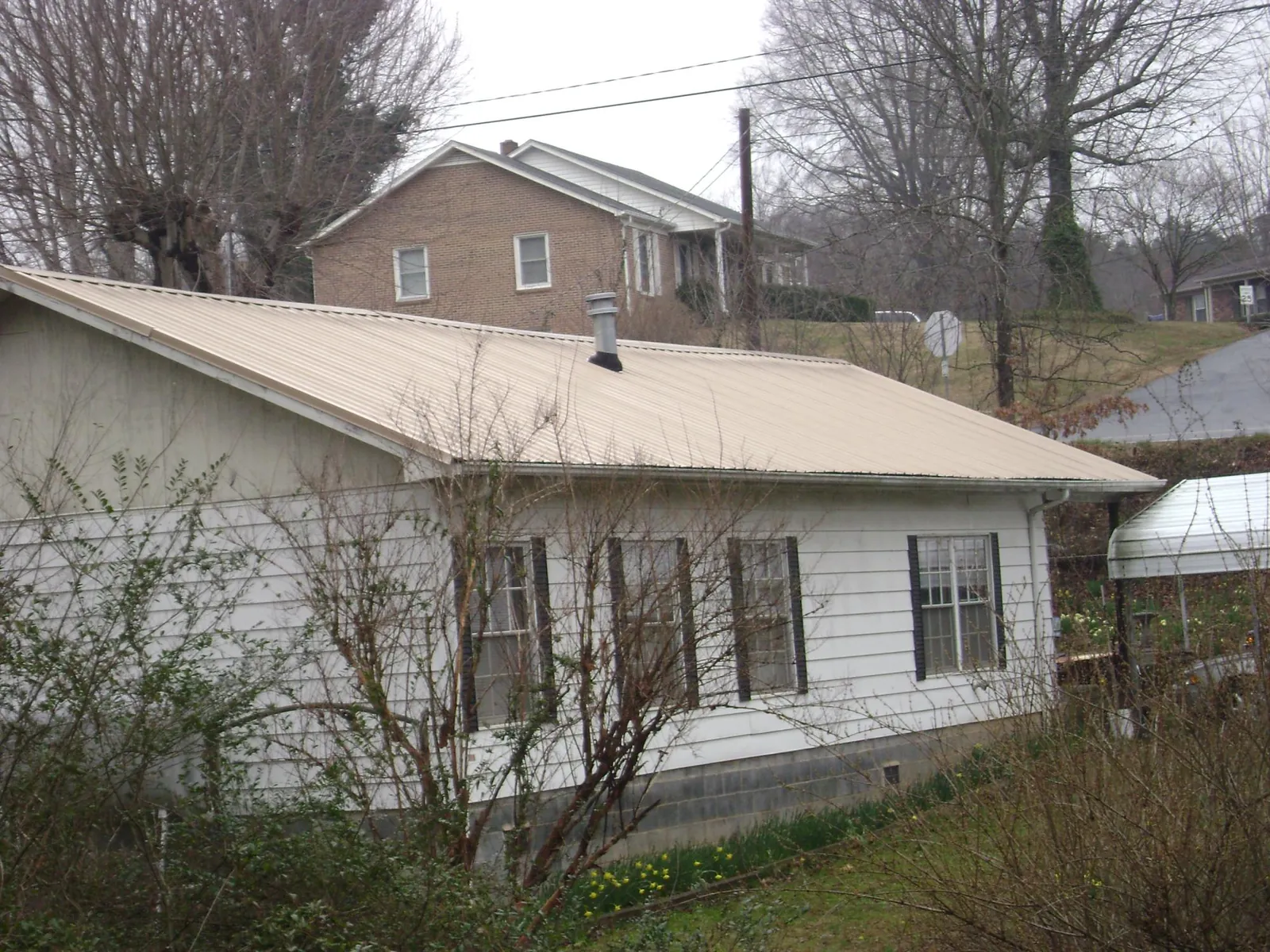 Tan metal roof on a white sided house set into a hillside — Commercial Roofing by Roofing Brothers in Elk Creek