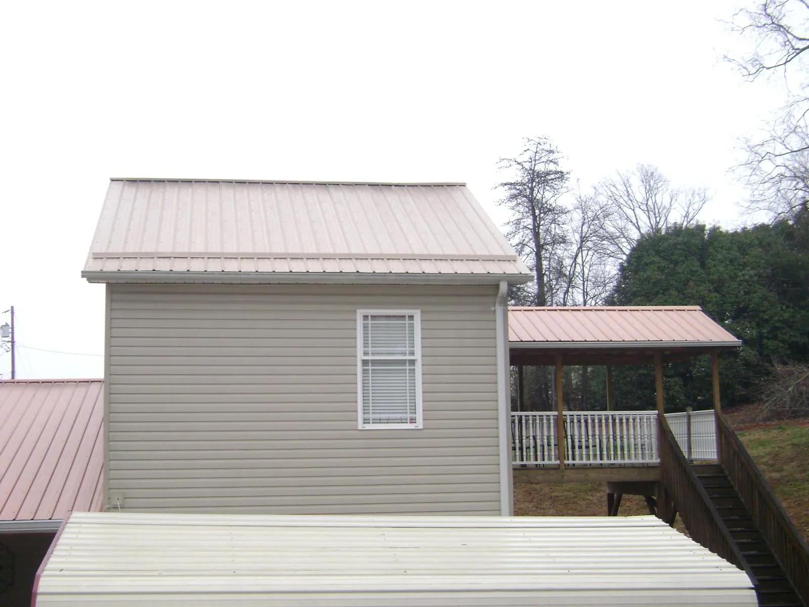Tan metal roofs on a two story addition and attached porch, from a Roof Replacement job in Elk Creek